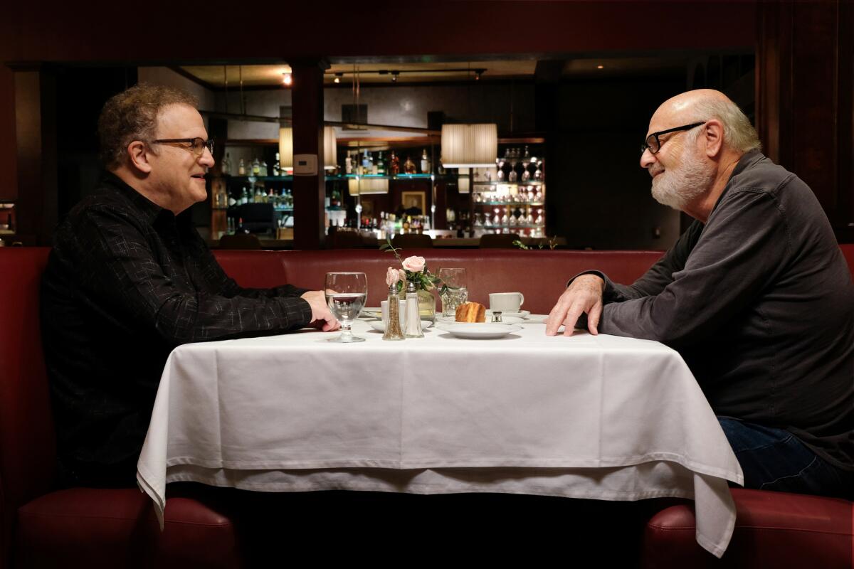 Two men converse at a dining table.