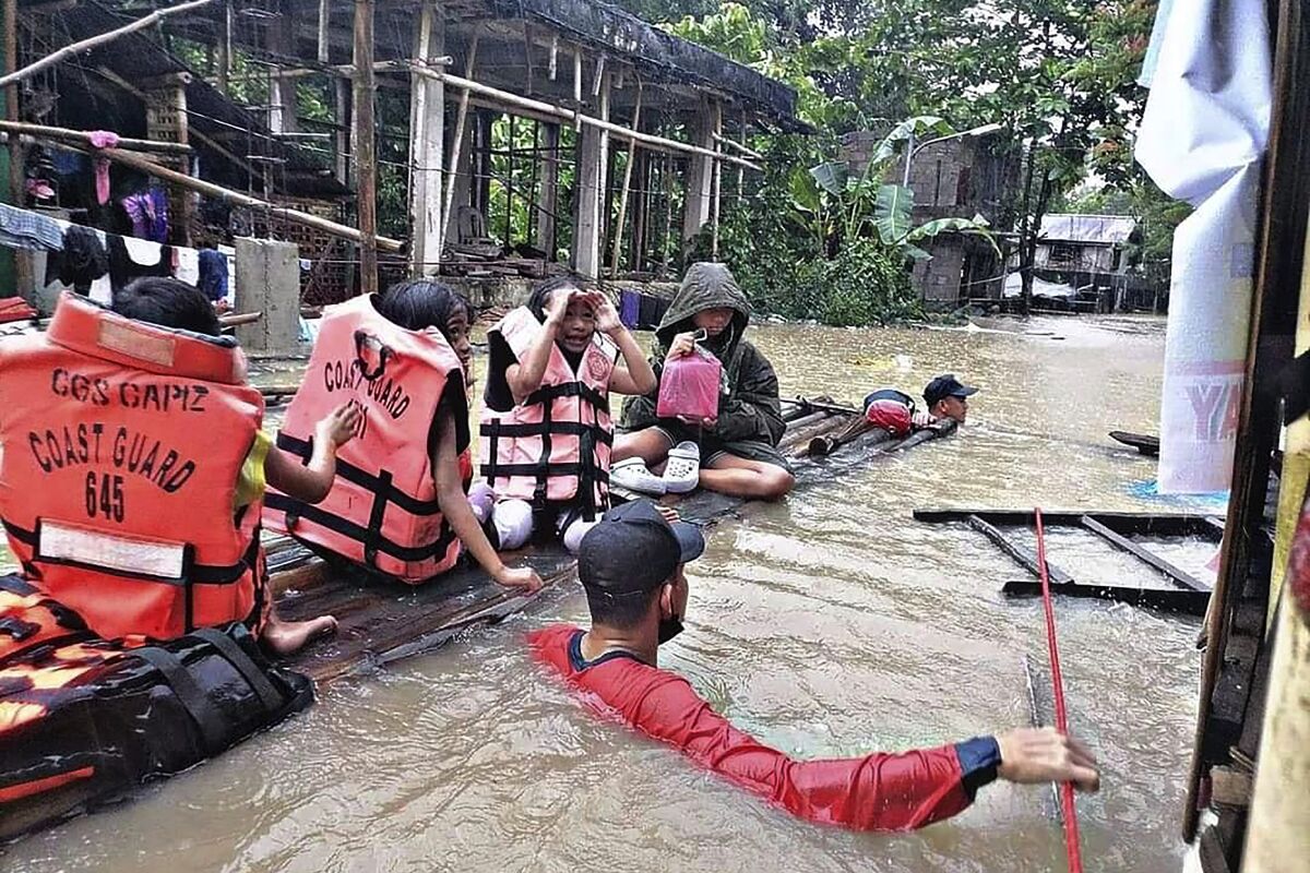 In this handout photo provided by the Philippine Coast Guard, residents are evacuated by rescuers in a flooded village in Panitan, Panay island, Philippines on Tuesday April 12, 2022. Heavy rains caused by a summer tropical depression killed at least several people in the central and southern Philippines, mostly due to landslides, officials said Monday. (Philippine Coast Guard via AP)