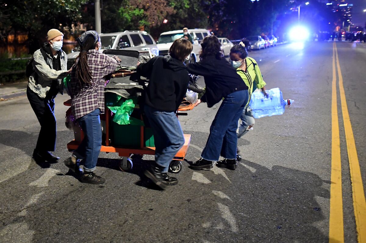 Supporters help a homeless woman evacuate as LAPD officers arrive in Echo Park Wednesday night to clear the encampment.