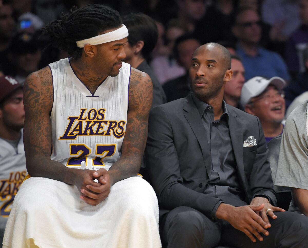 Lakers center Jordan Hill and injured shooting guard Kobe Bryant look at each other on the bench during the first half of the Lakers' 100-93 loss to the Mavericks.