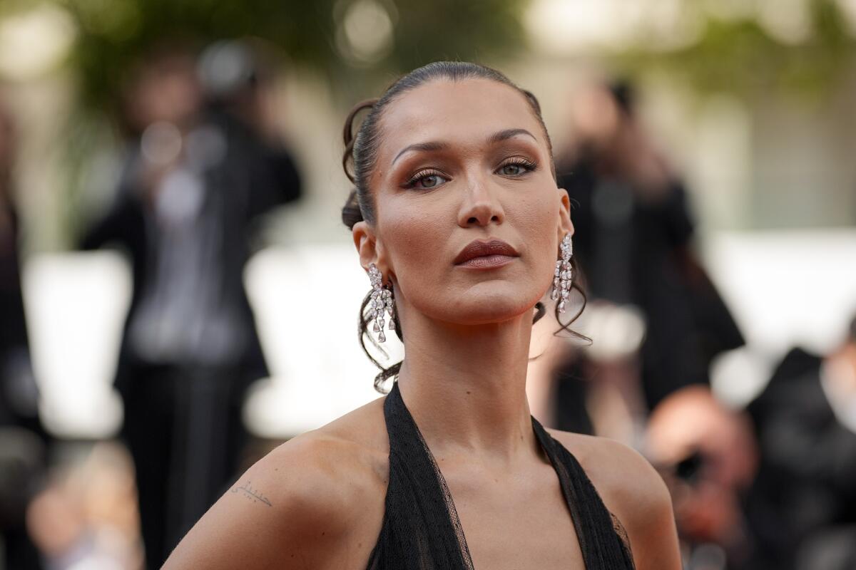 Bella Hadid posing with her dark hair pulled back and dangly earrings. 