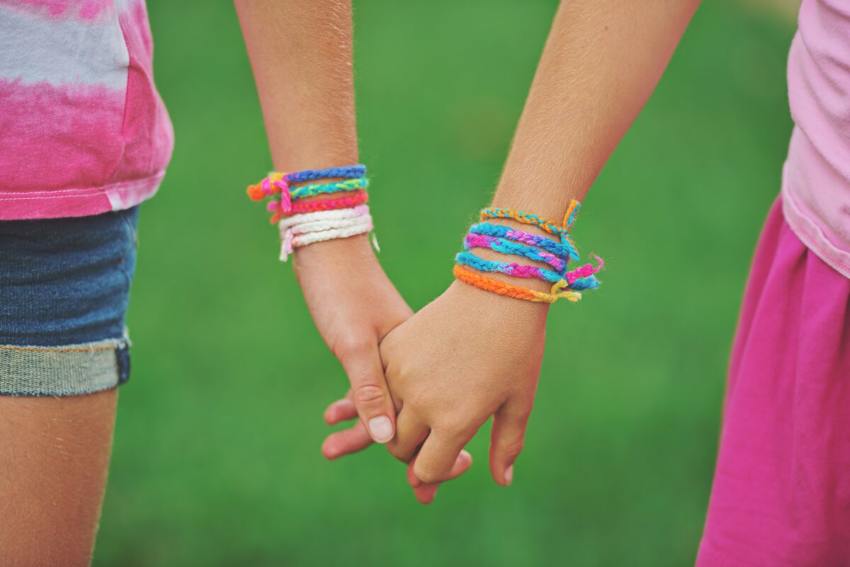 A close-up of two girls holdings hands while wearing friendship bracelets made from colorful yarn 