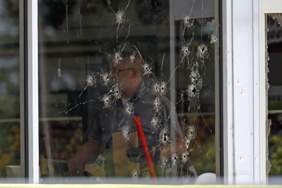 More than 20 holes pock a window as law enforcement officers inside work the scene of a shooting.