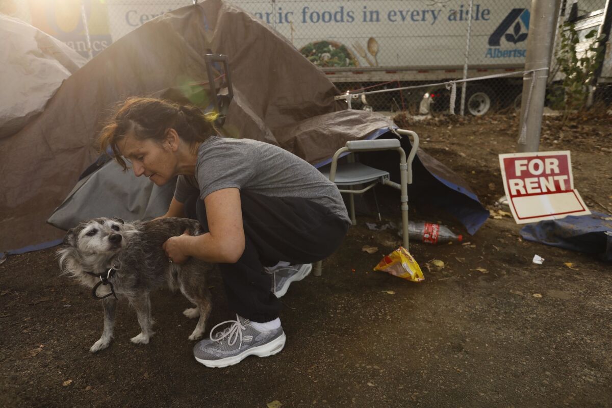 Melissa Millner, 46, pets her dog Lazy next to her tent that rests between a bike path and the 5 Freeway in Los Angeles. Millner, who has been homeless for 12 years, shares the encampment with others.