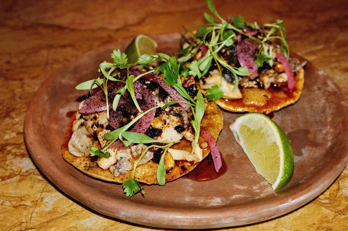 Two small mushroom and huitlacoche tostadas topped with cilantro, side of lime wedge, on ceramic plate at Barr Seco