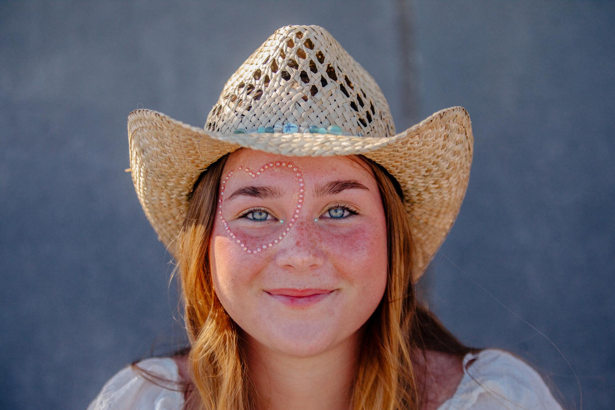 A portrait of a girl wearing a cowboy hat with a jewel heart around her eye.