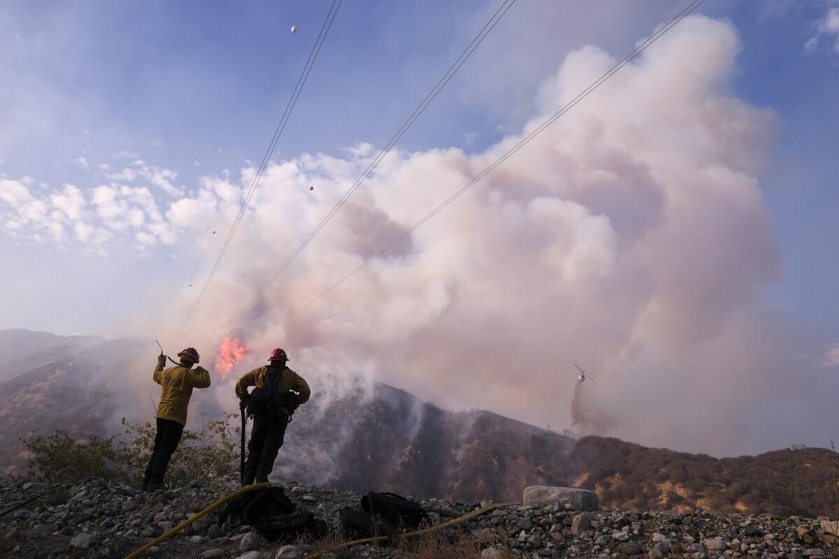 Firefighters watch as a helicopter drops water