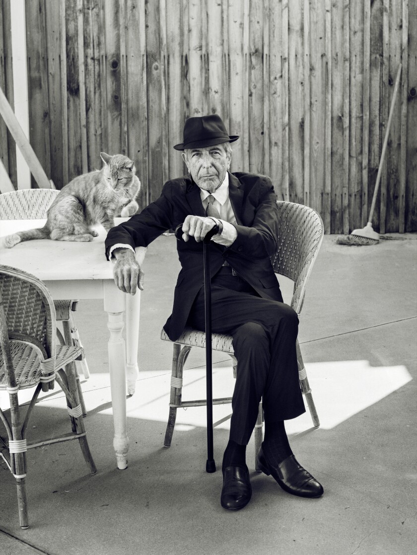 A man in a suit and hat sits outside next to a cat.