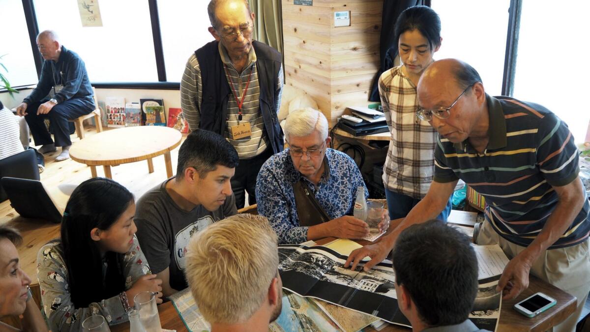 Kazuhiko Futagawa shows pictures of the atomic bombing's aftermath to the Saperstein family at Social Book Cafe as Soh Horie, another survivor, looks on.