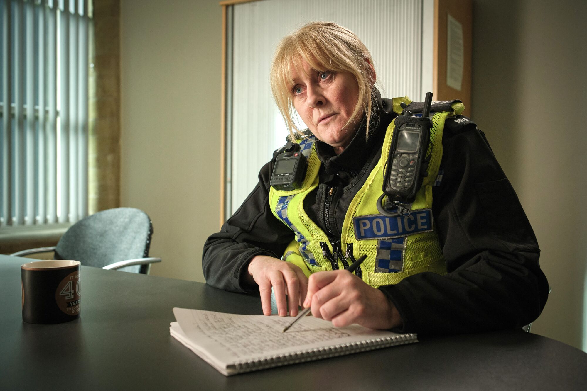 A female police officer sits in an interrogation room taking notes.