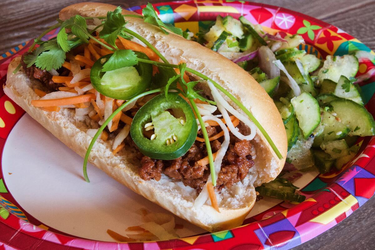 A vegan Impossible bánh bì sandwich with lemongrass cucumber salad on a colorful paper plate.