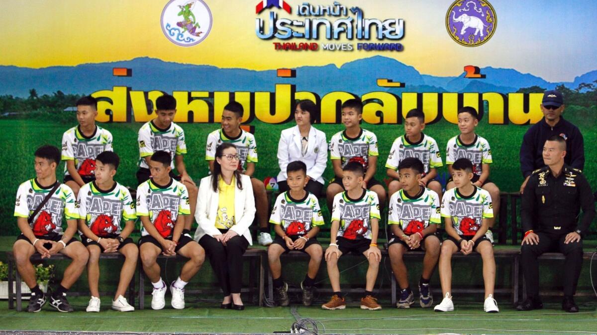 Twelve rescued members of the Wild Boar soccer team and their assistant coach sit with Thai health officers and soldiers in their first public appearance on July 18.