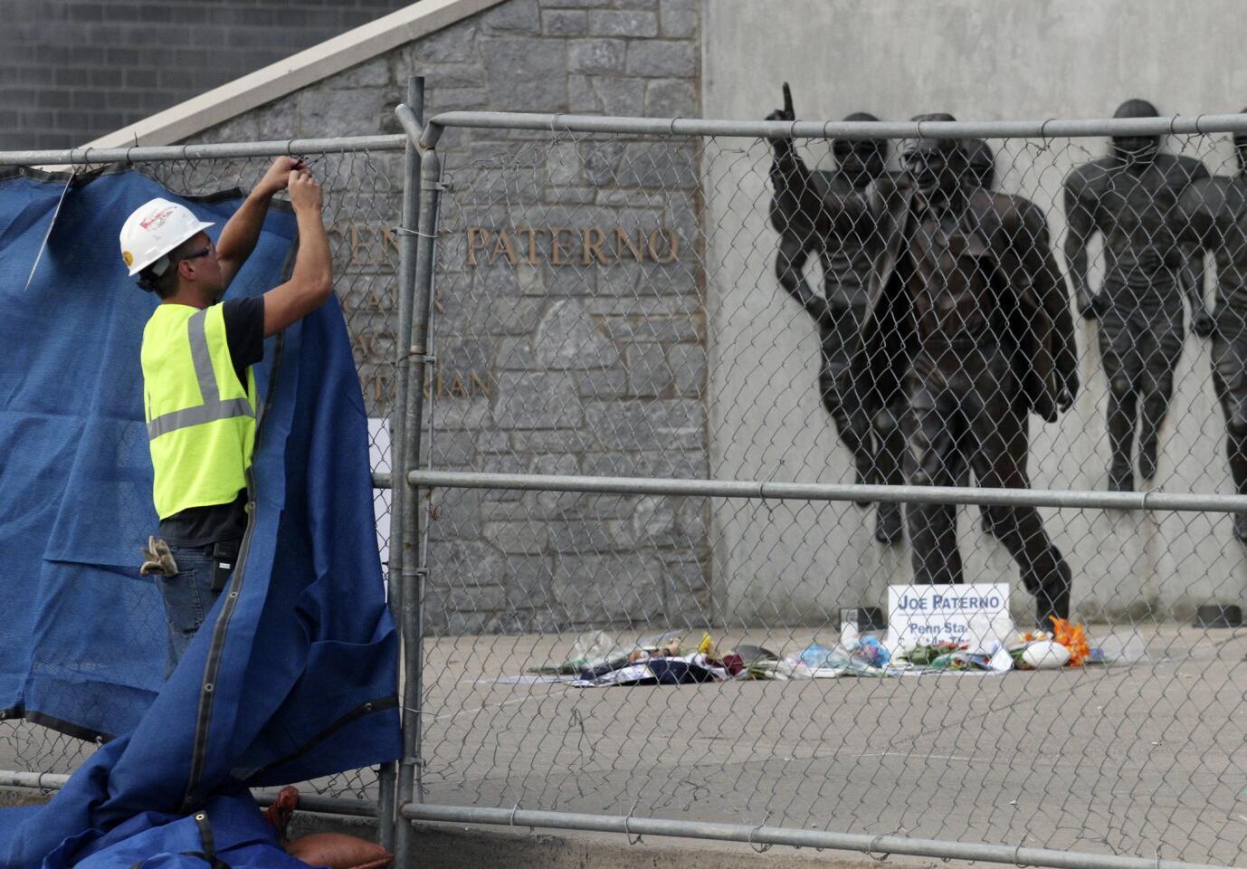 A worker puts up tarps on a temporary fence around the statue of the late Penn State football coach Joe Paterno before removing the statue outside Beaver Stadium in State College, Pennsylvania, July 22, 2010. The removed statue was placed it inside the stadium early Sunday, moments after the university president announced the school's intention to remove it.