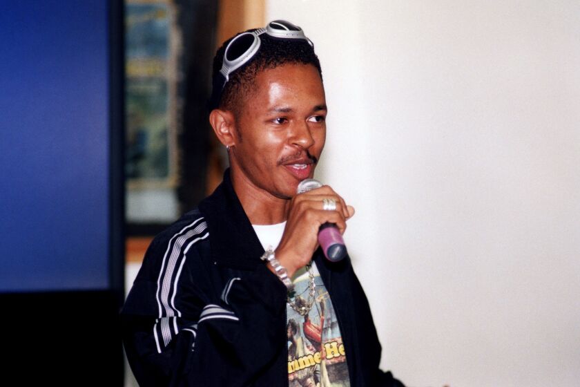 A singer with sunglasses on his head holds a microphone in his right hand while performing