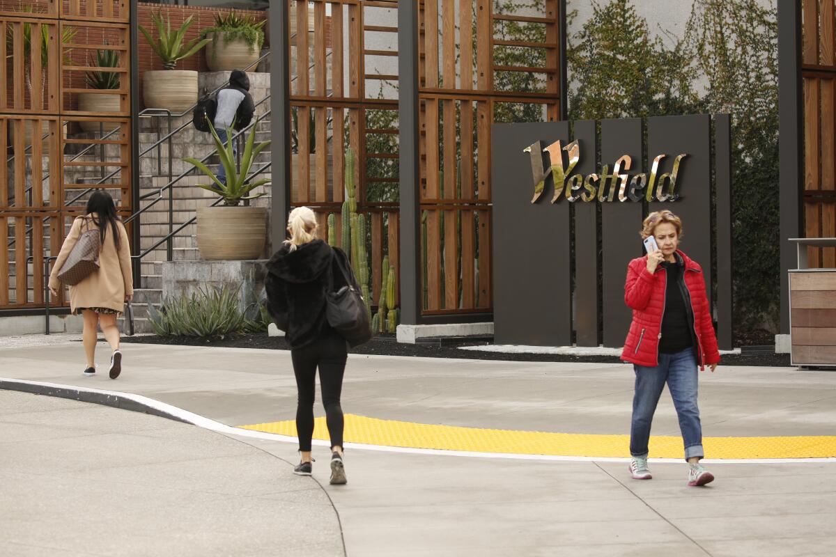 Pedestrians walk past a Westfield sign.