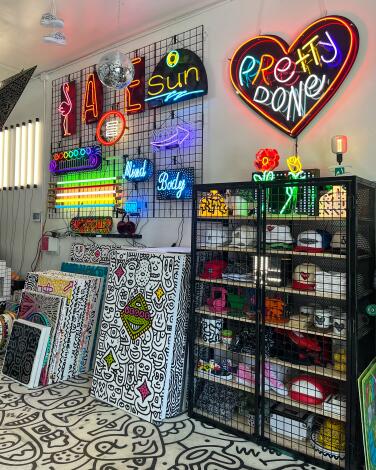A neon heart with the words Pretty Done hangs on a wall above and near art supplies