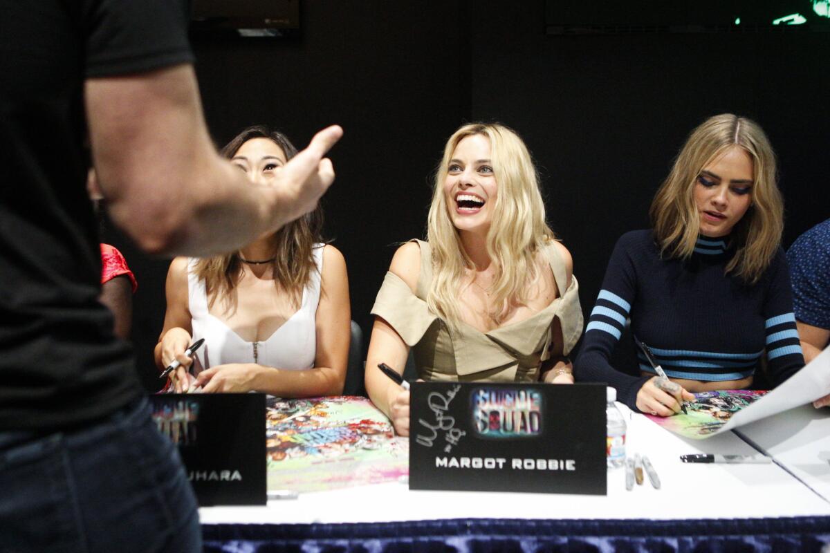 "Suicide Squad" star Margot Robbie laughs and autographs posters for the upcoming film in the Exhibition Hall during Comic-Con International in San Diego.