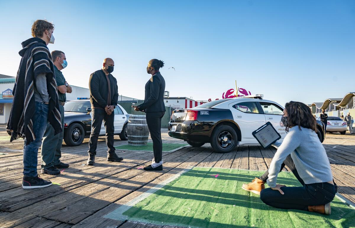 Actors wearing face masks stand near police cars on the set of the CBS show “NCIS: Los Angeles”  