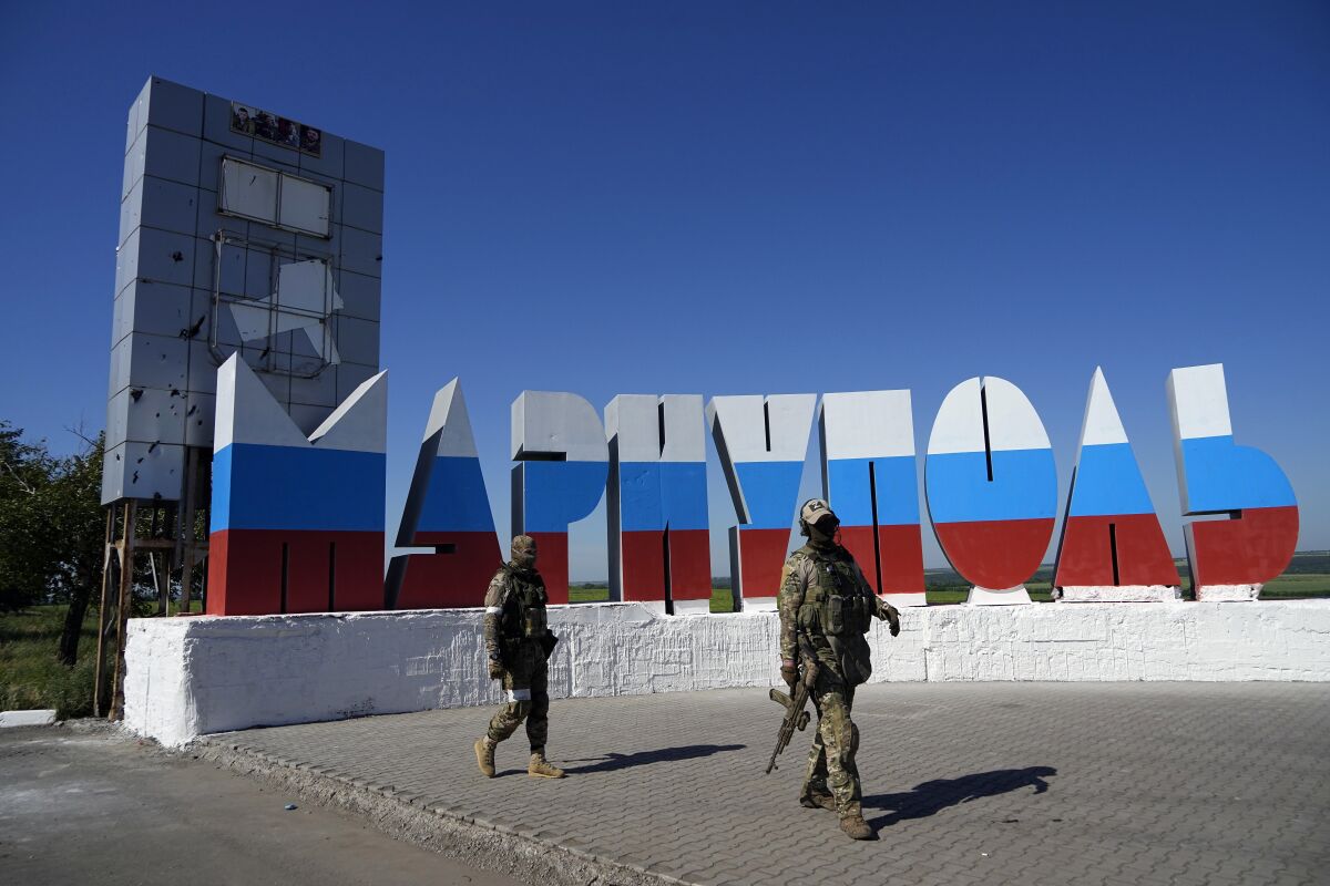 Soldados rusos pasan frente al nombre de la ciudad Mariúpol repintado con los colores de la bandera rusa 