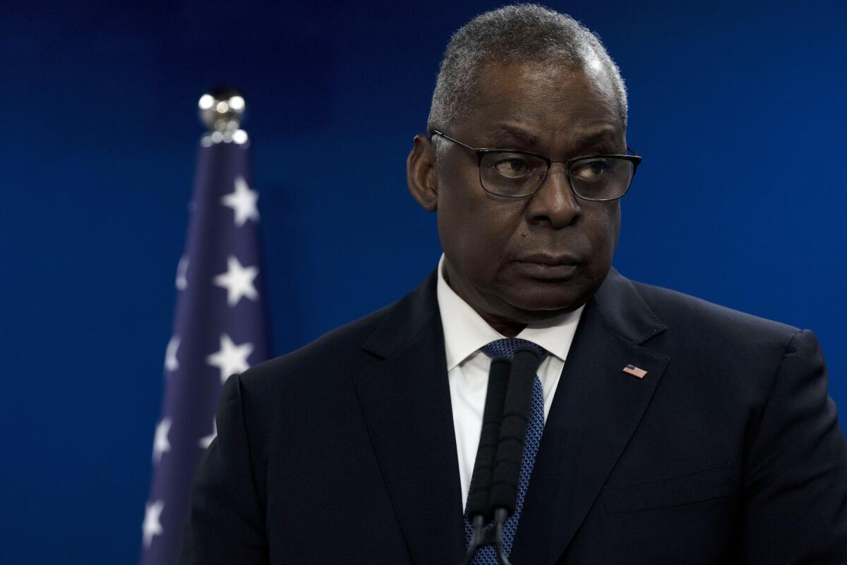 U.S. Secretary of Defense Lloyd Austin stands in front of a U.S. flag and looks to the side.