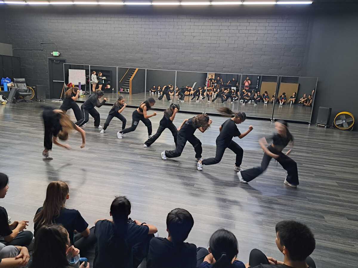 Dancers thrust forward in formation in a dance studio. 