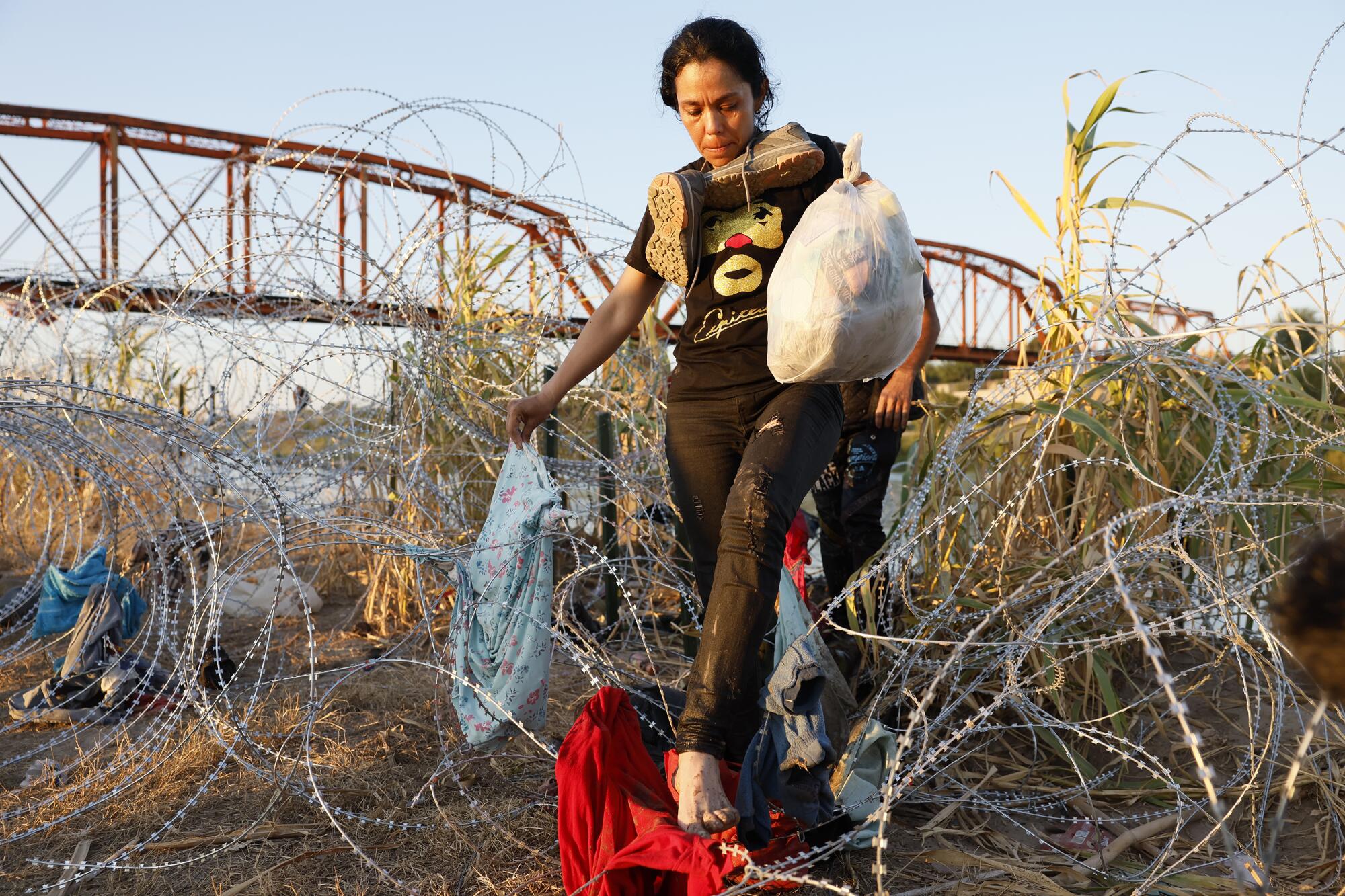 A barefoot woman carefully steps on a piece of fabric covering a stretch of razor wire.