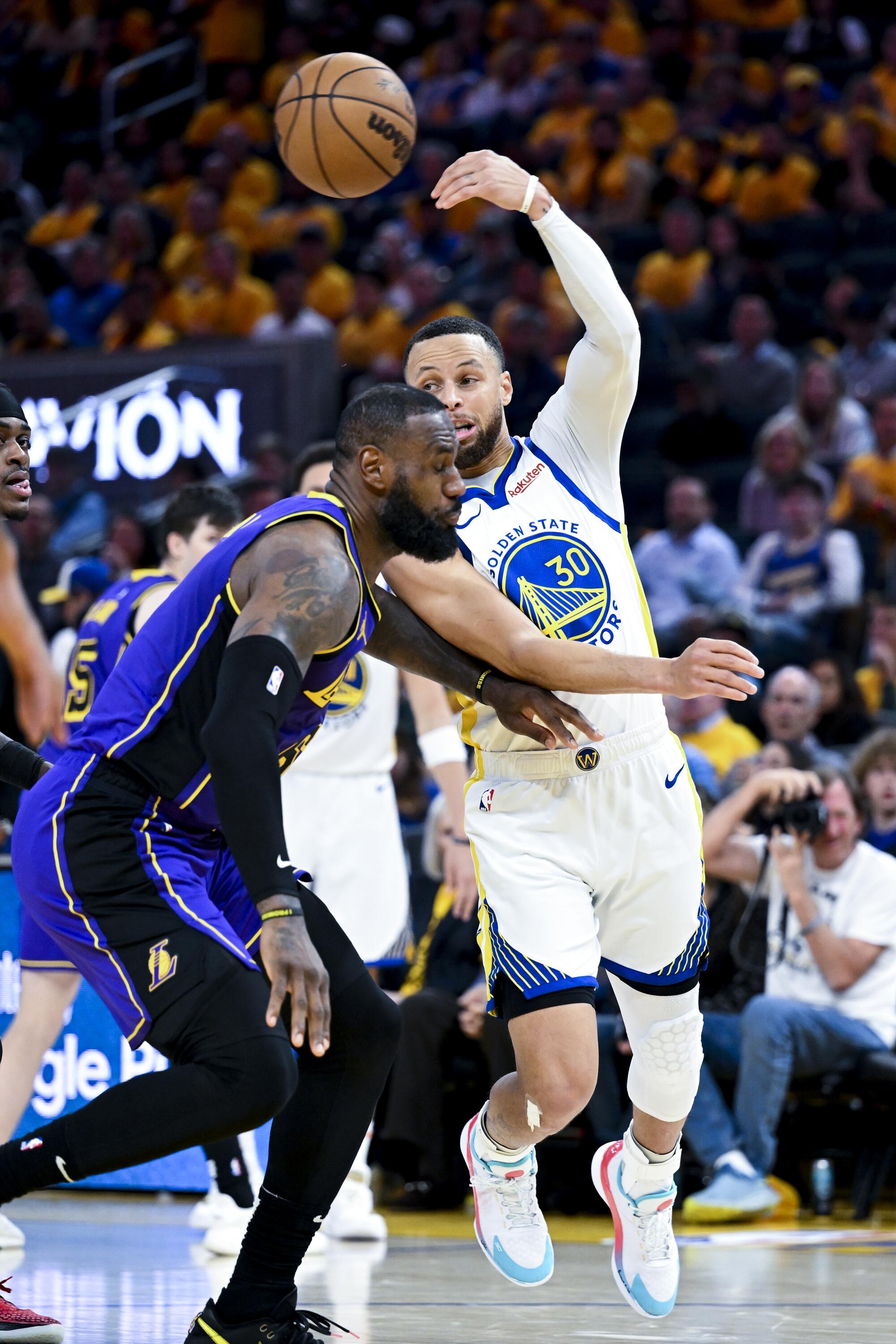 Golden State Warriors guard Stephen Curry, right, passes the ball as Lakers forward LeBron James defends.