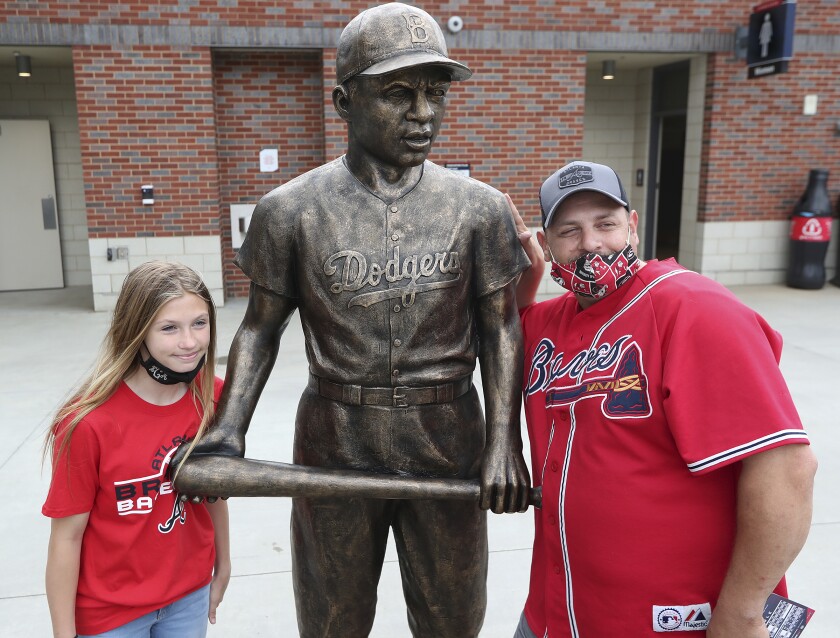 Atlanta Braves fans Pete Ciccarello and his daughter Haley pause for a photo with the statue of Jackie Robinson on Jackie Robinson Day prior to a baseball game between the Miami Marlins and Atlanta Braves in Atlanta, Thursday, April 15, 2021. (Curtis Compton/Atlanta Journal-Constitution via AP)