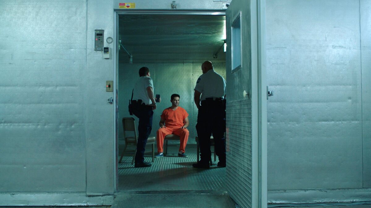 In a scene from "The Infiltrators," a man named Beni is seen in orange jumpsuit inside a metal-walled cell.