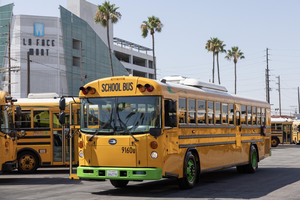 An electric L.A. school bus is stopped in a bus parking lot.