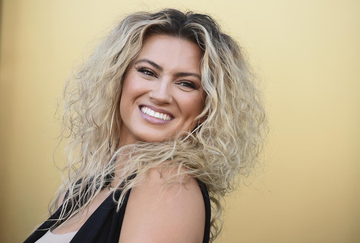 Tori Kelly smiles in a black-and-white outfit against a yellow backdrop.