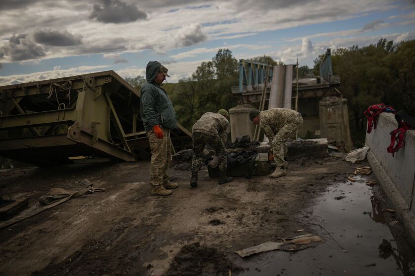 Ukrainian soldiers remove metal pieces as they work on a bridge damaged during fighting with Russian troops in Izium, Ukraine, Monday, Oct. 3, 2022. (AP Photo/Francisco Seco)