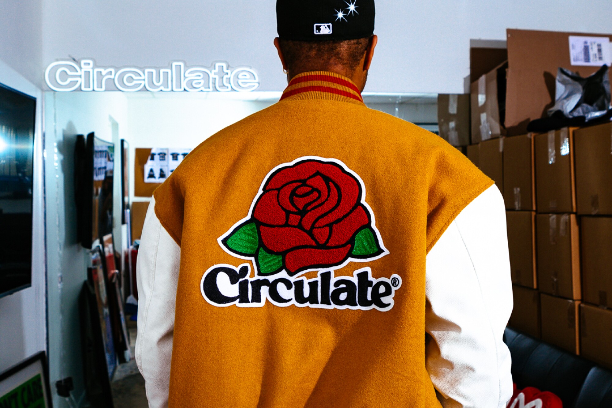 Streetwear designer seen from behind wearing an orange jacket with a red rose and the word "Circulate" on it.