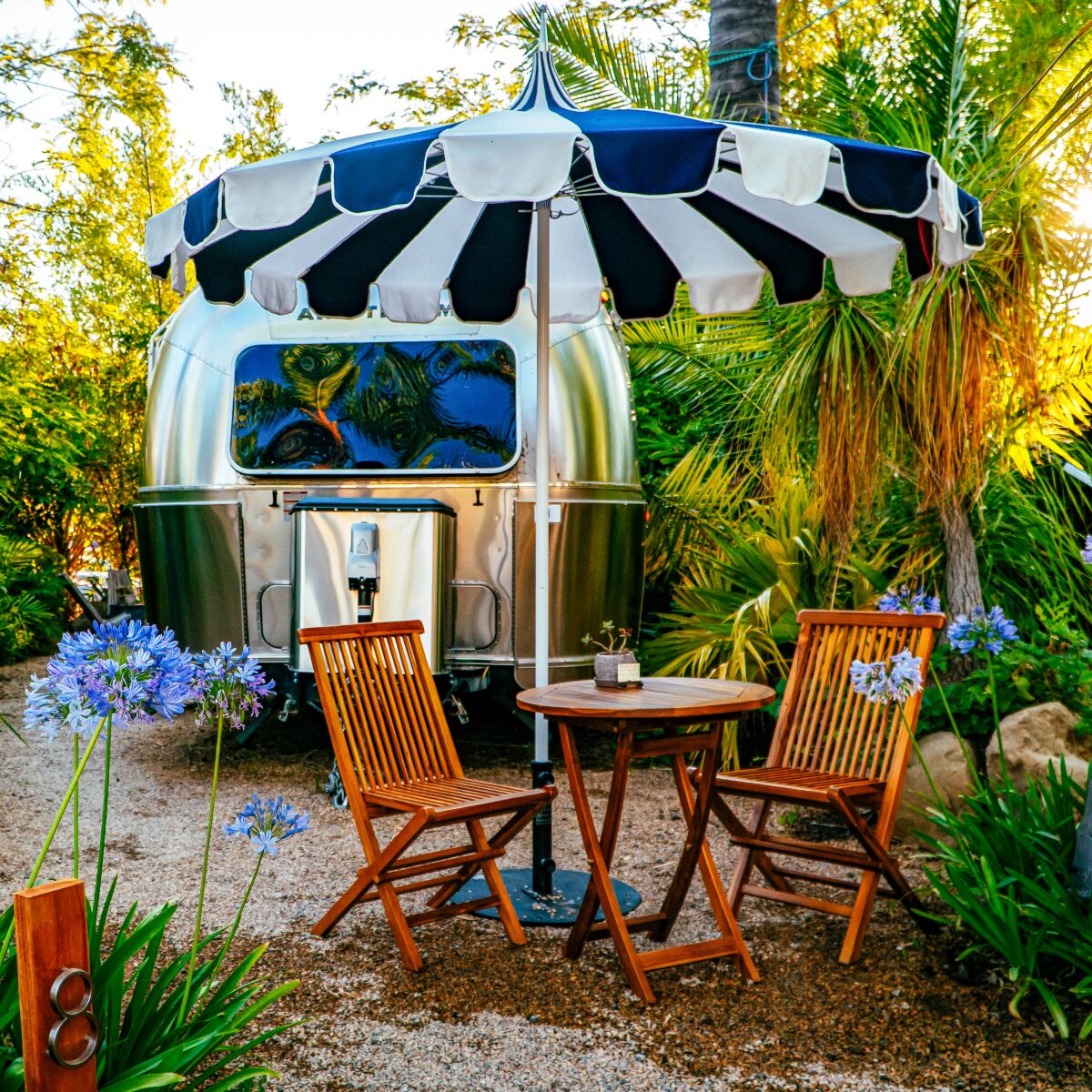 An Airstream trailer with chairs, a table and an umbrella.