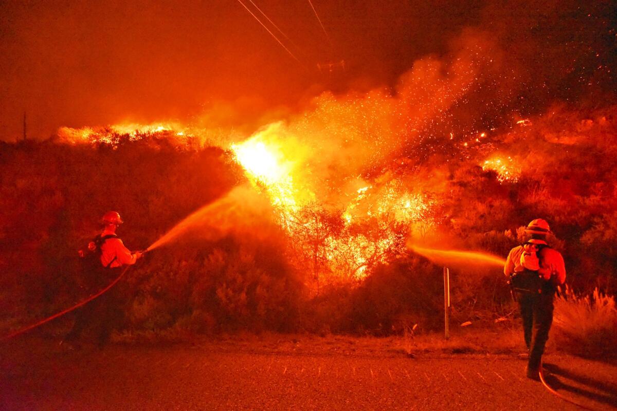 Firefighters knock down flames from the Alisal fire while standing in the northbound lanes of the 101 Freeway.