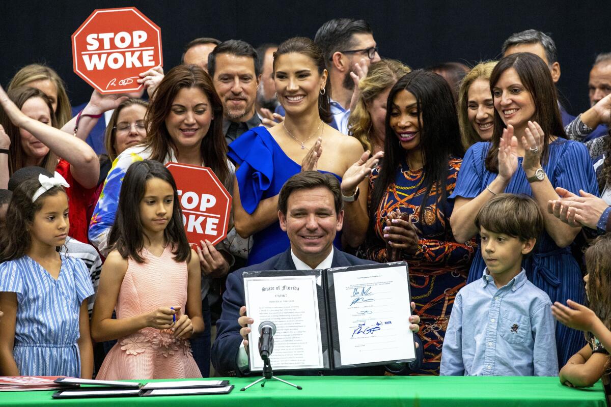 Florida Gov. Ron DeSantis holds up a bill he signed alongside children and supporters holding signs reading "Stop Woke."