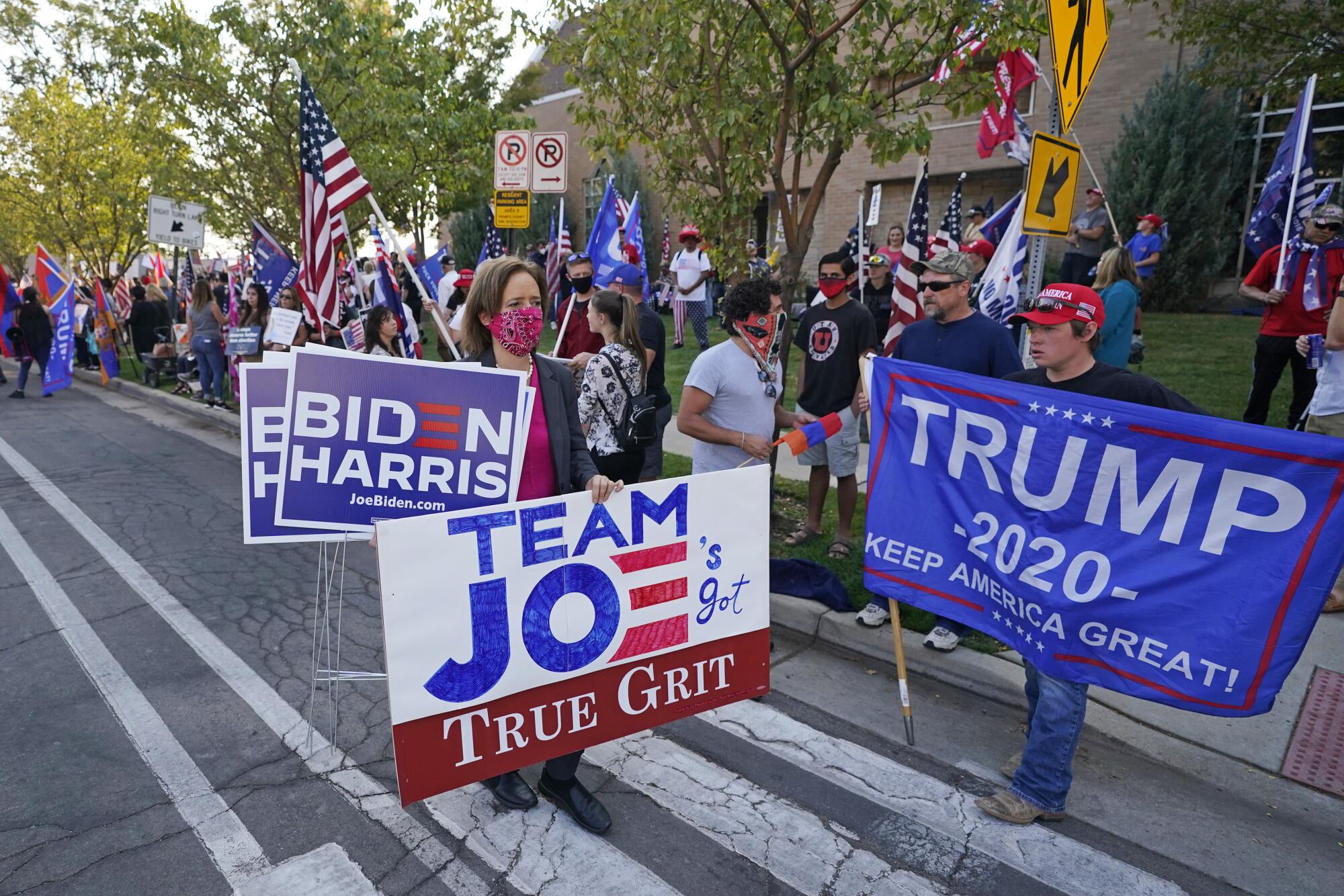 Demonstrators hold signs reading Biden-Harris, Team Joe's Got True Grit and Trump 2020 Keep America Great