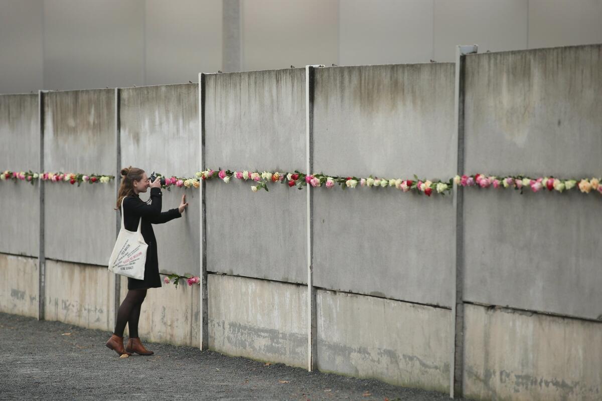 A young woman photographs flowers at a remnant of the Berlin Wall on the 26th anniversary of its fall.