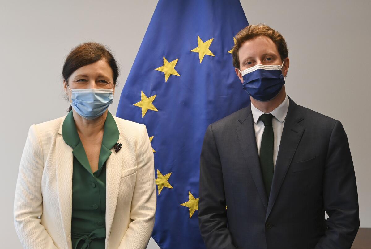 A woman and a man wearing masks stand before a European Union flag