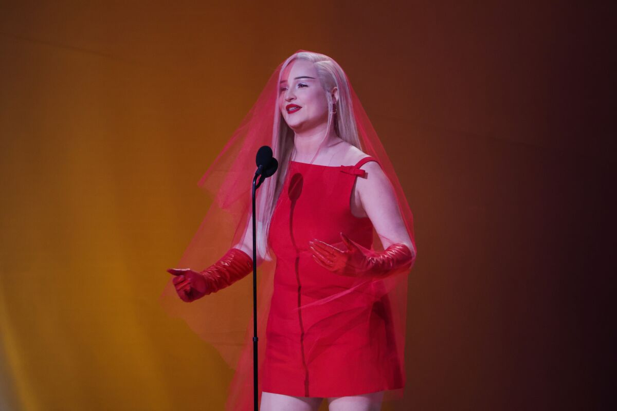 A woman in a red dress speaks onstage