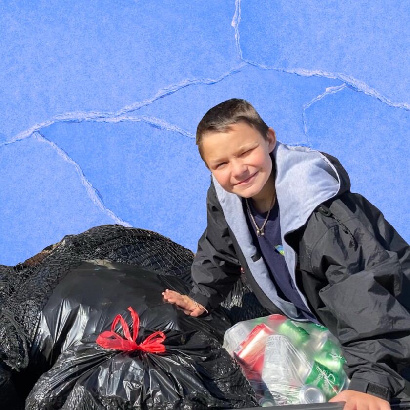 An adolescent boy smiles as he poses for a photo leaning over trash bags full of aluminum cans.