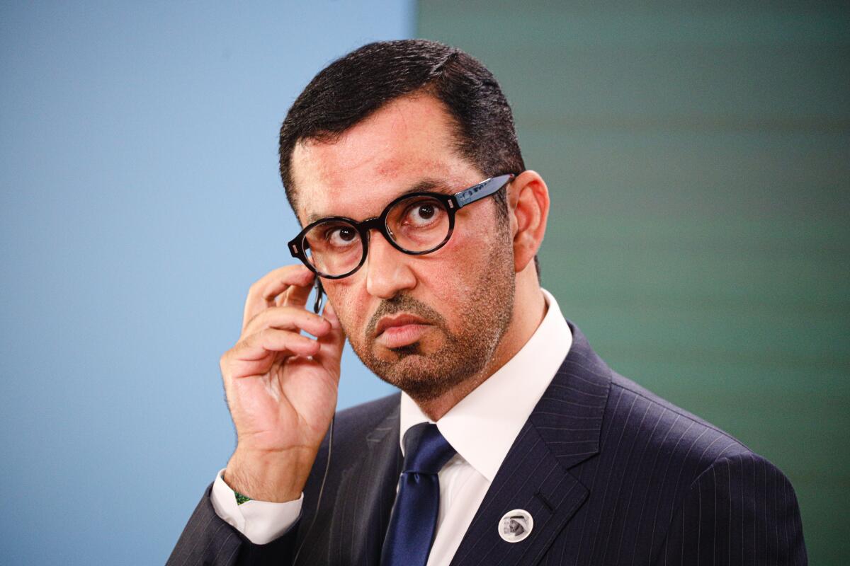 A head-and-shoulder horizontal frame of Sultan Al Jaber, wearing a dark suit and tie and round glasses