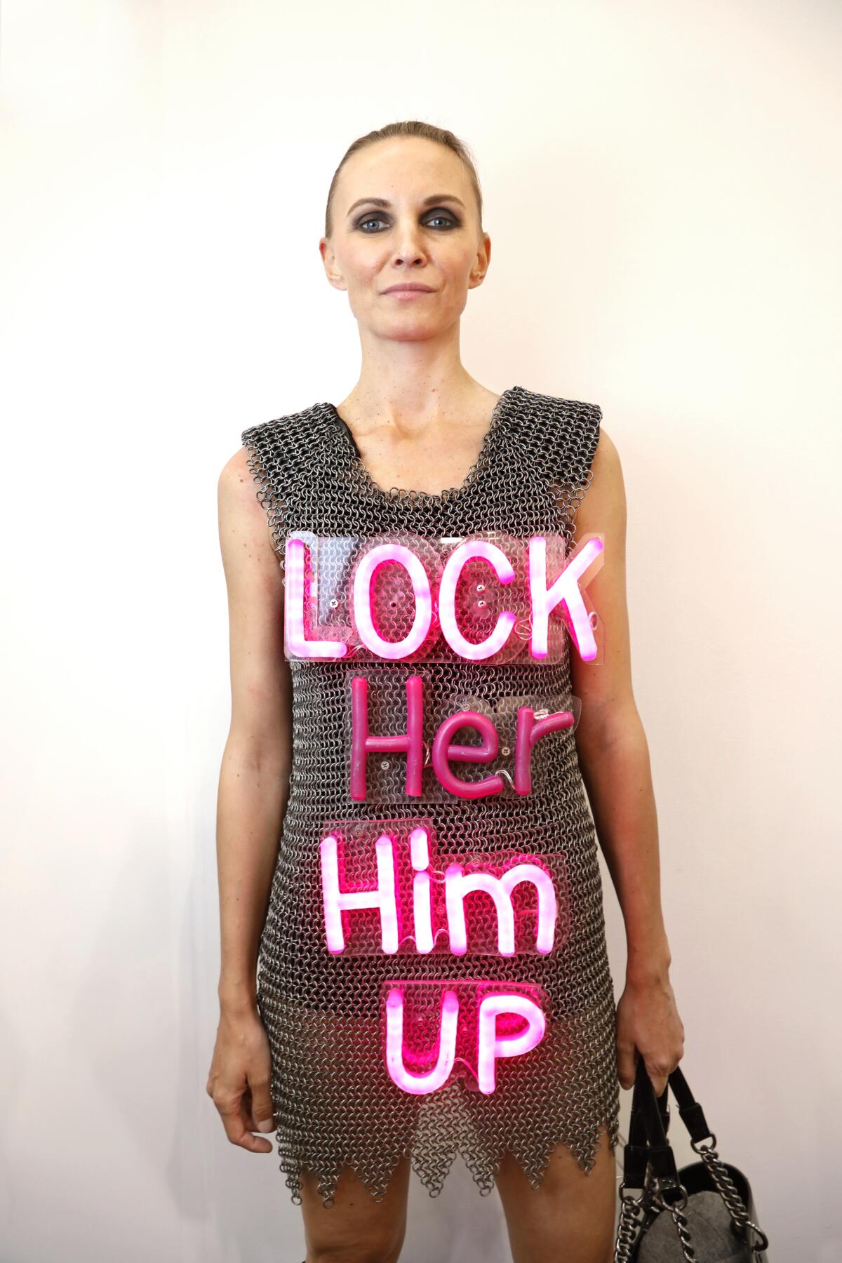 Gordana Simunovic wears an installation art dress at Frieze Los Angeles: chain-mail style with the words "Lock Her Him Up" in neon pink and "Lock Him Up" lit up.