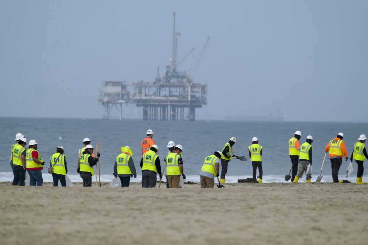 Workers clean a contaminated part of Huntington Beach, Calif. in October with an oil platform in the background 