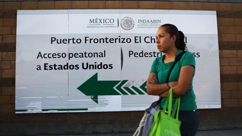A woman stands at the El Chapparal port of entry, with a sign pointing toward the U.S., earlier this year in Tijuana.