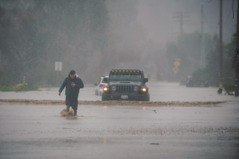 San Diego, California - January 22: Heavy rains flood both sides of the border. A man walks out his stranded car at the Tijuana River Valley on Monday, Jan. 22, 2024 in San Diego, California. (Alejandro Tamayo / The San Diego Union-Tribune)