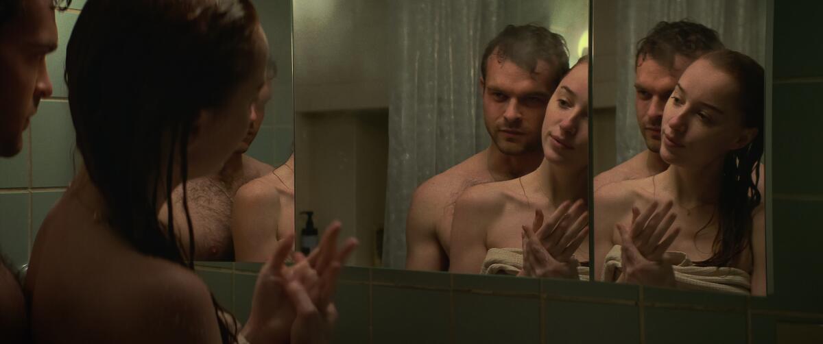 A man and a woman, having just taken a shower, stand in front of a bathroom mirror.