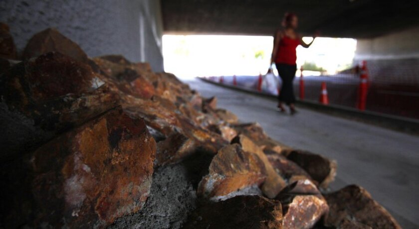 A woman walks past stones and rocks that the city recently installed on Imperial Avenue below an overpass of the 5 Freeway to deter homeless encampments on the street.