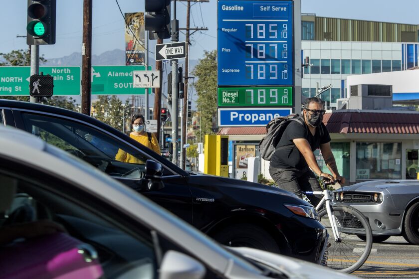 LOS ANGELES, CA-JUNE 1,2022:A bicycle rider maneuvers around motorists stuck in traffic on Cesar E. Chavez Ave., at the intersection of Alameda Street in downtown Los Angeles, where the price of gasoline approaches close to $8 a gallon at the Chevron gas station. (Mel Melcon / Los Angeles Times)