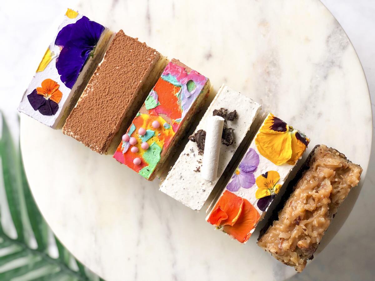 A top-down photo of a diagonal row of colorful, icing-painted rectangular cake bars from bakery Flouring LA.